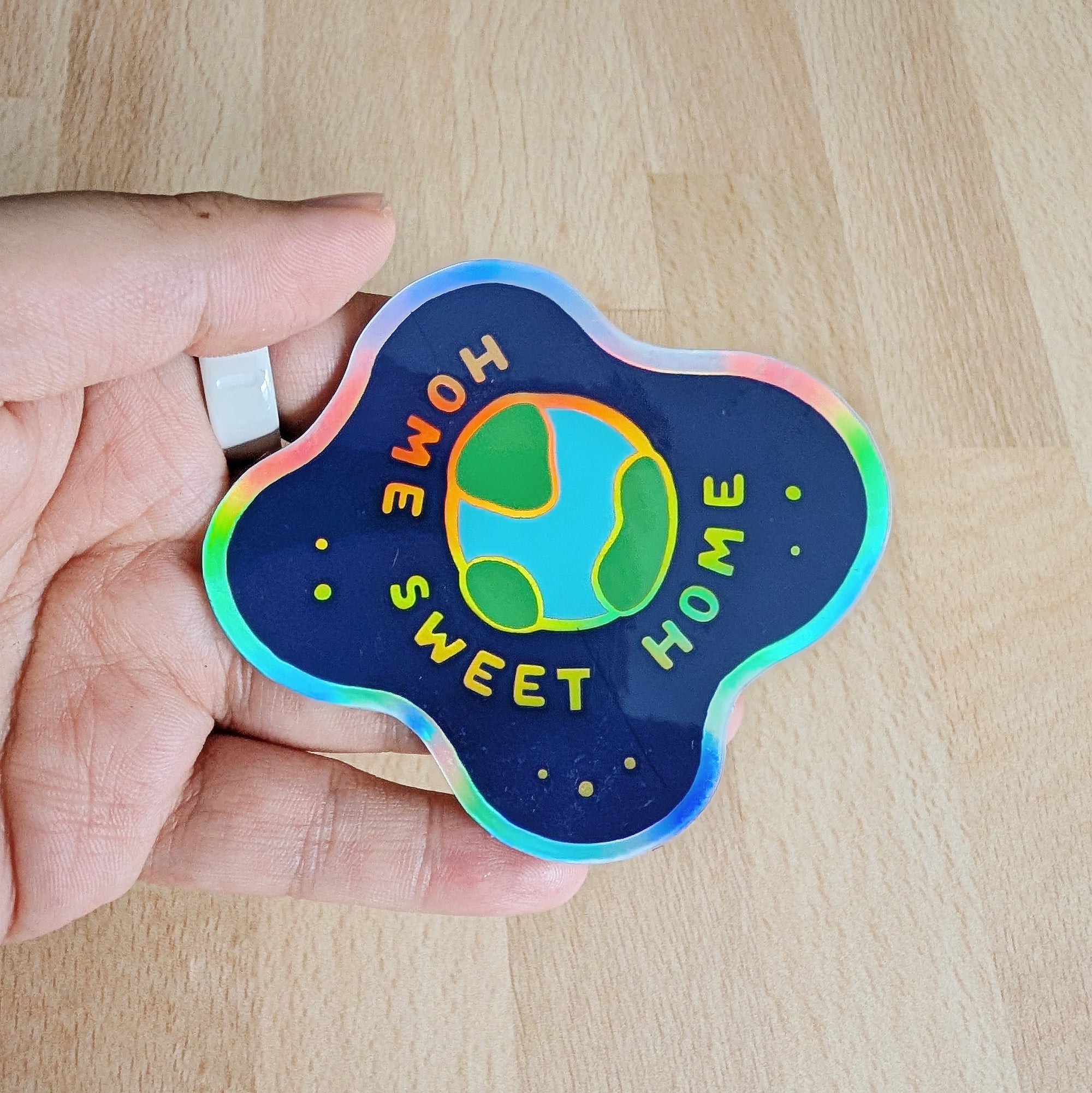 Holographic vinyl sticker featuring planet earth floating in space with the words Home Sweet Home, held in a hand
