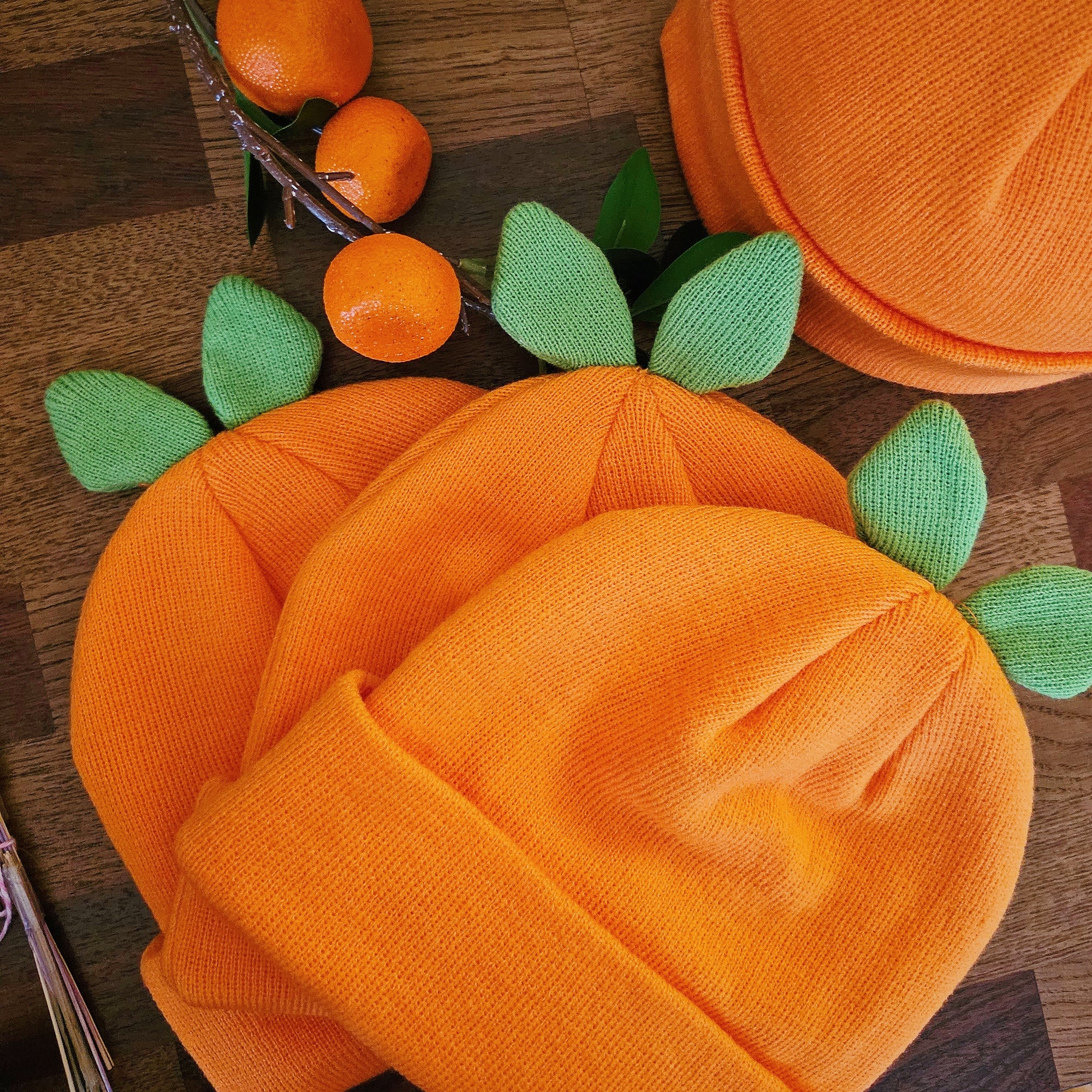 Three orange misomomo leaf sprout beanies, laid flat on top of each other on a wooden surface. 