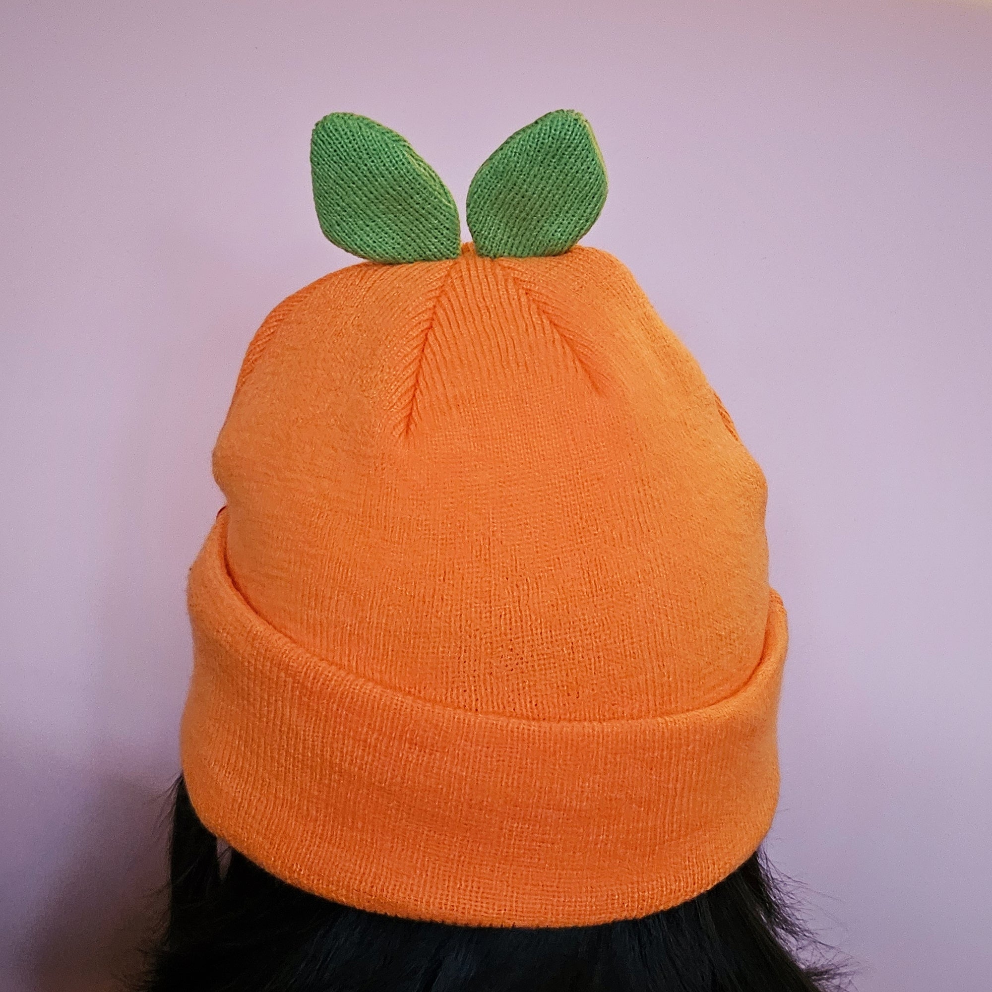 Misomomo orange leaf sprout beanie with two leaves on the top part, pictured on a head to show the fit.