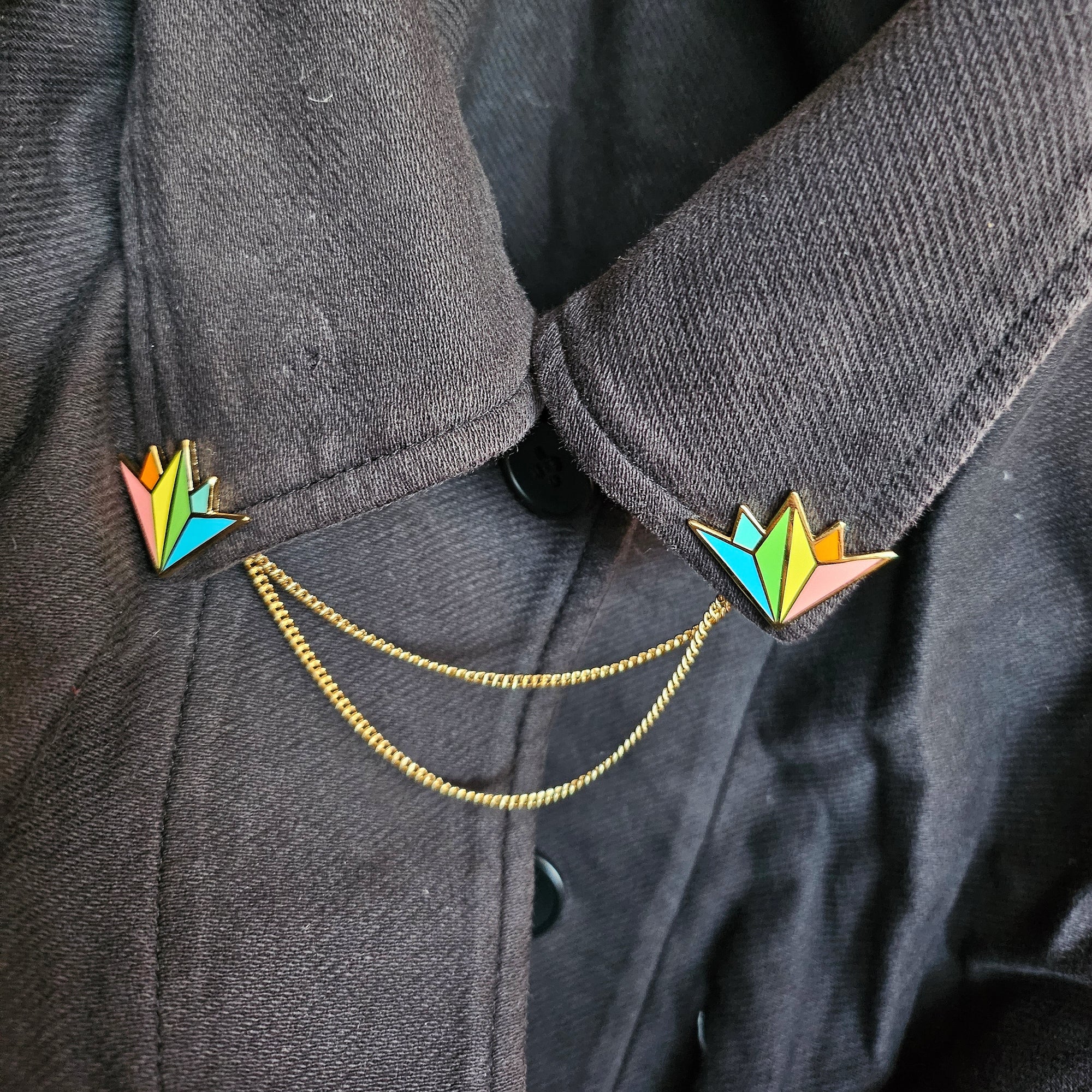 pair of misomomo rainbow collar pins shown on a black jacket with the optional gold double chain attachment. the collar pins fit perfectly into the corner of the collar and add a pop of rainbow.