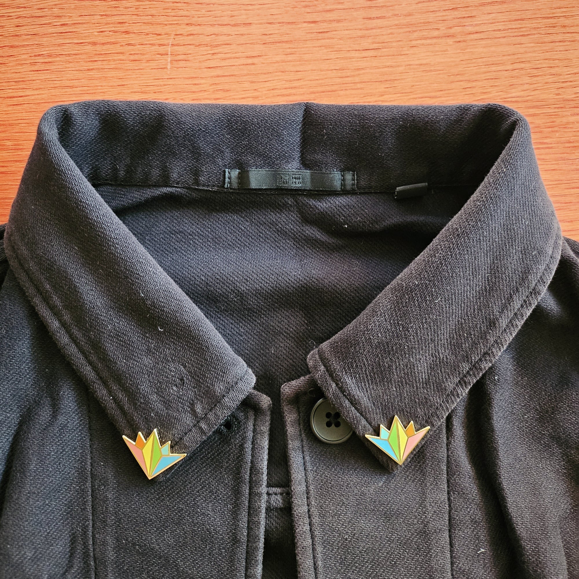 pair of misomomo rainbow collar pins shown on a black jacket. the collar pins fit perfectly into the corner of the collar and add a pop of rainbow.