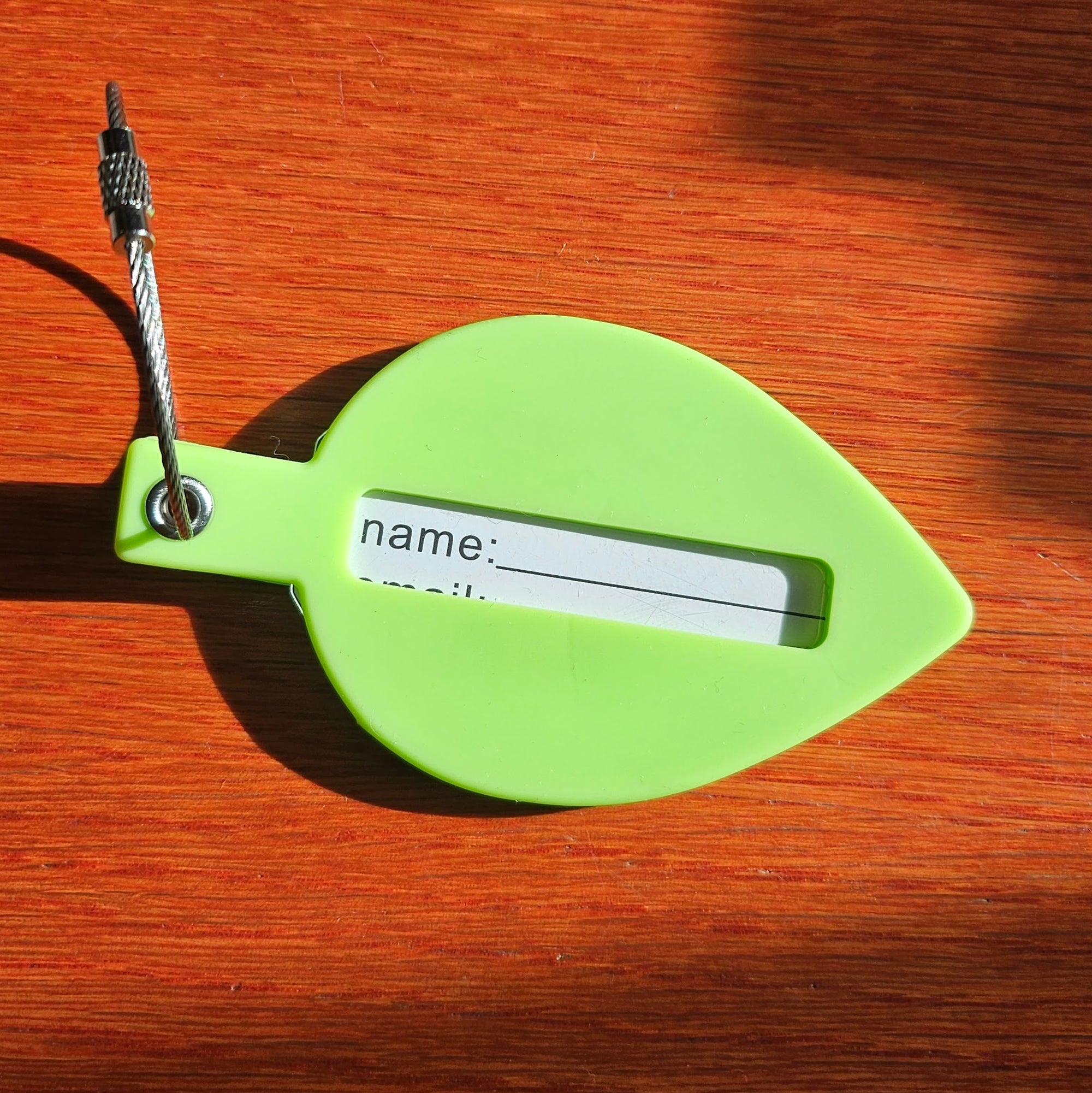 A green silicone leaf shaped luggage tag with a privacy cutout and a paper tag to write your name and personal info