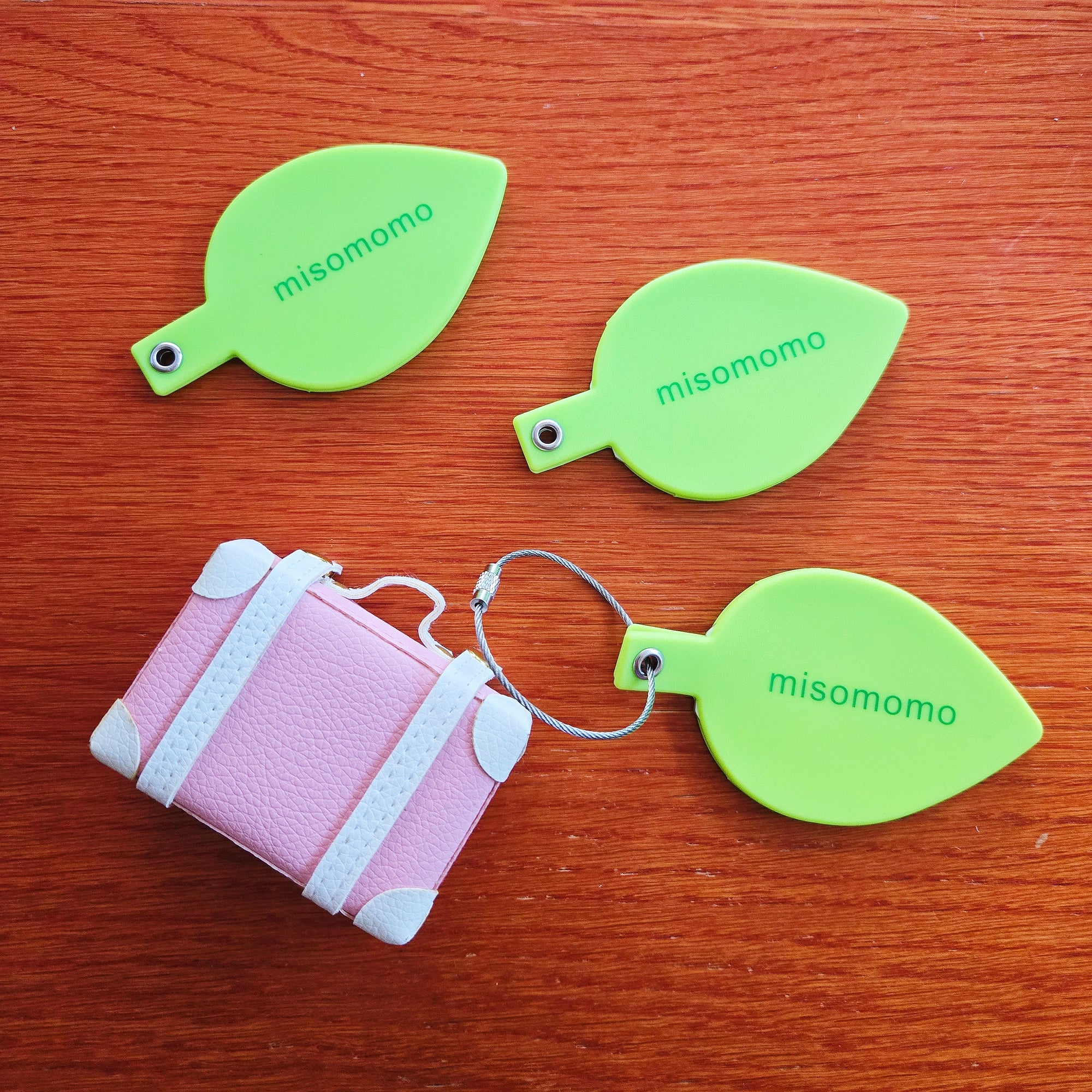Three misomomo leaf shaped silicone luggage tags next to a cute tiny suitcase