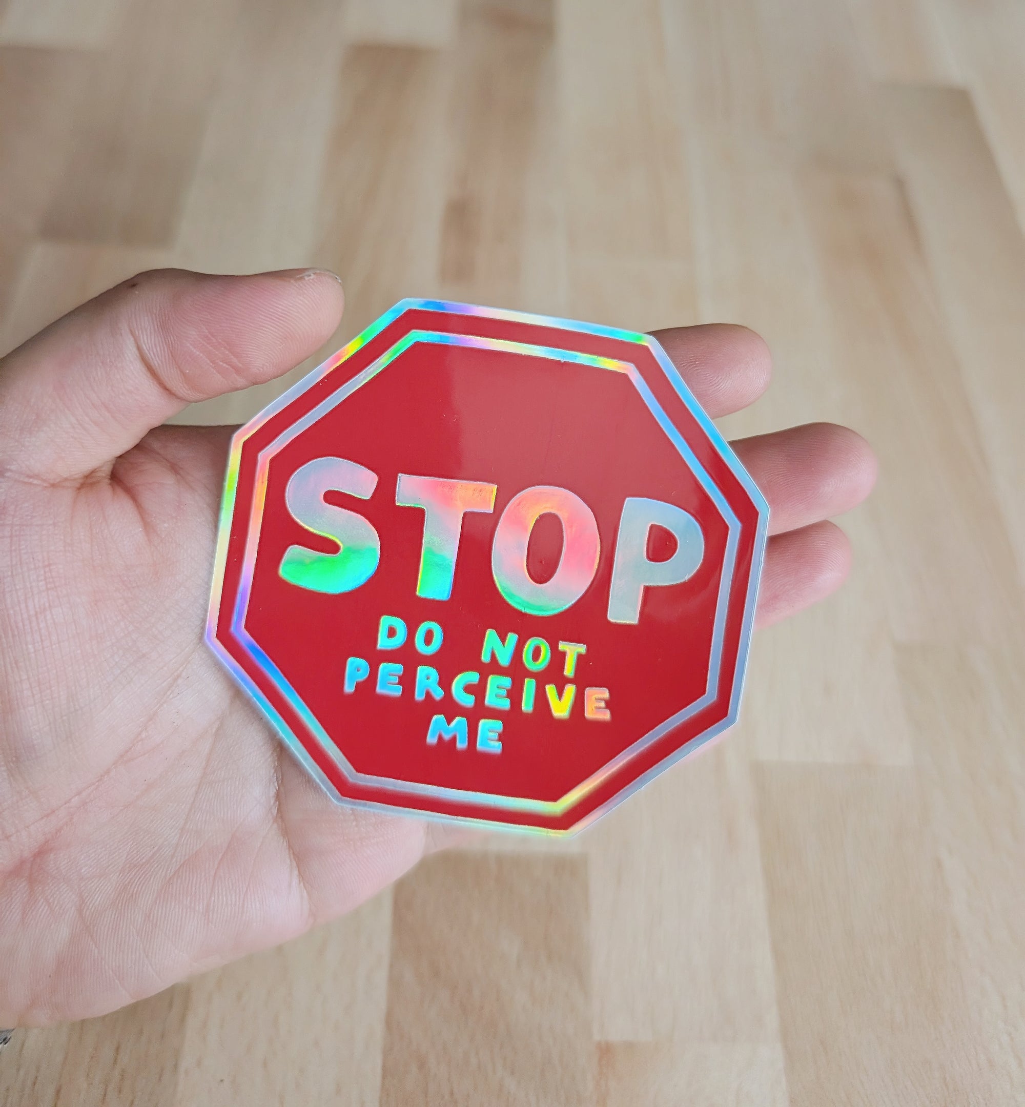 vinyl sticker of a red stop sign saying "STOP do not perceive me", held in a hand