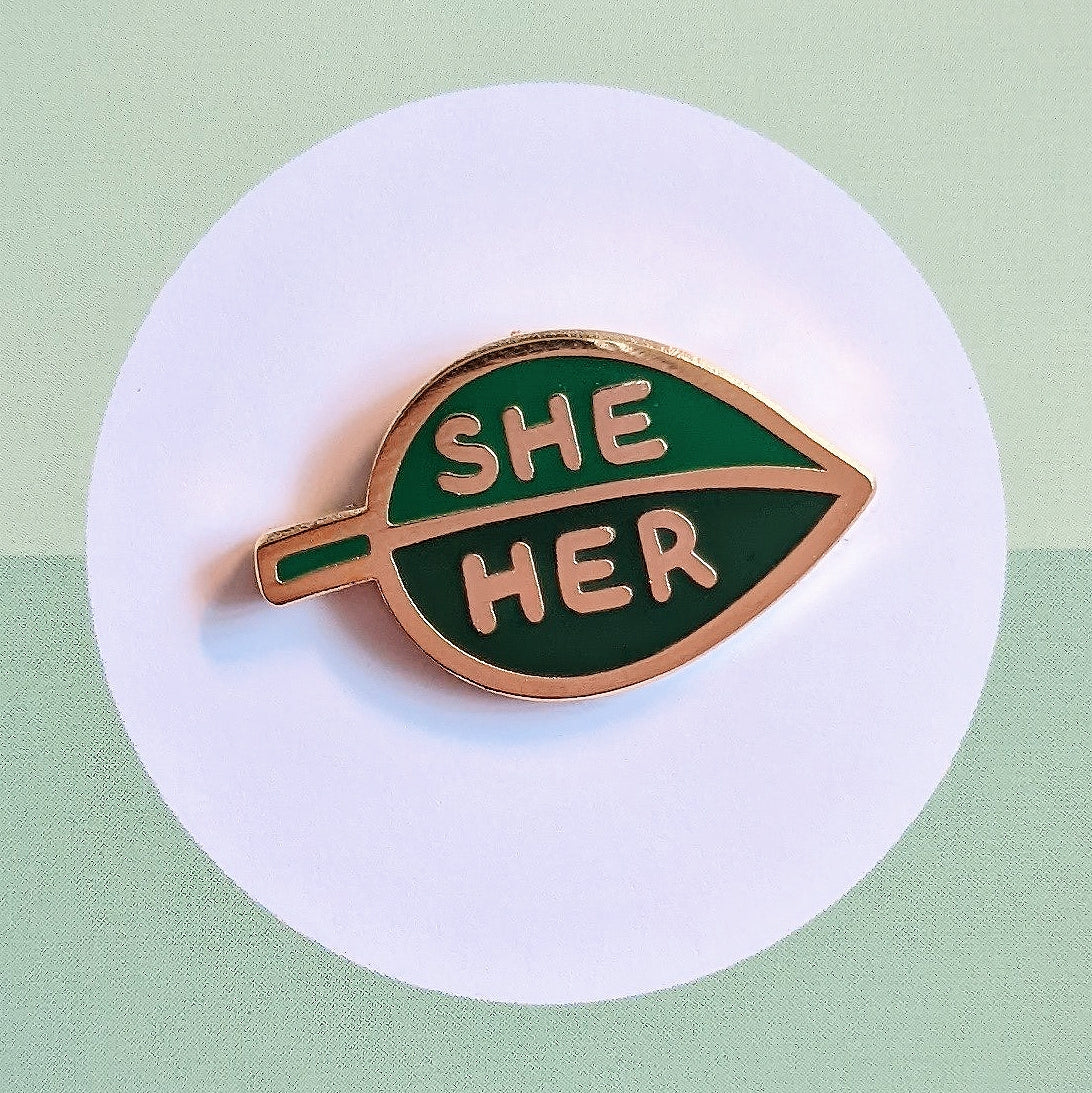 misomomo leaf shaped enamel pronoun pin in two tones of green, featuring she/her pronouns