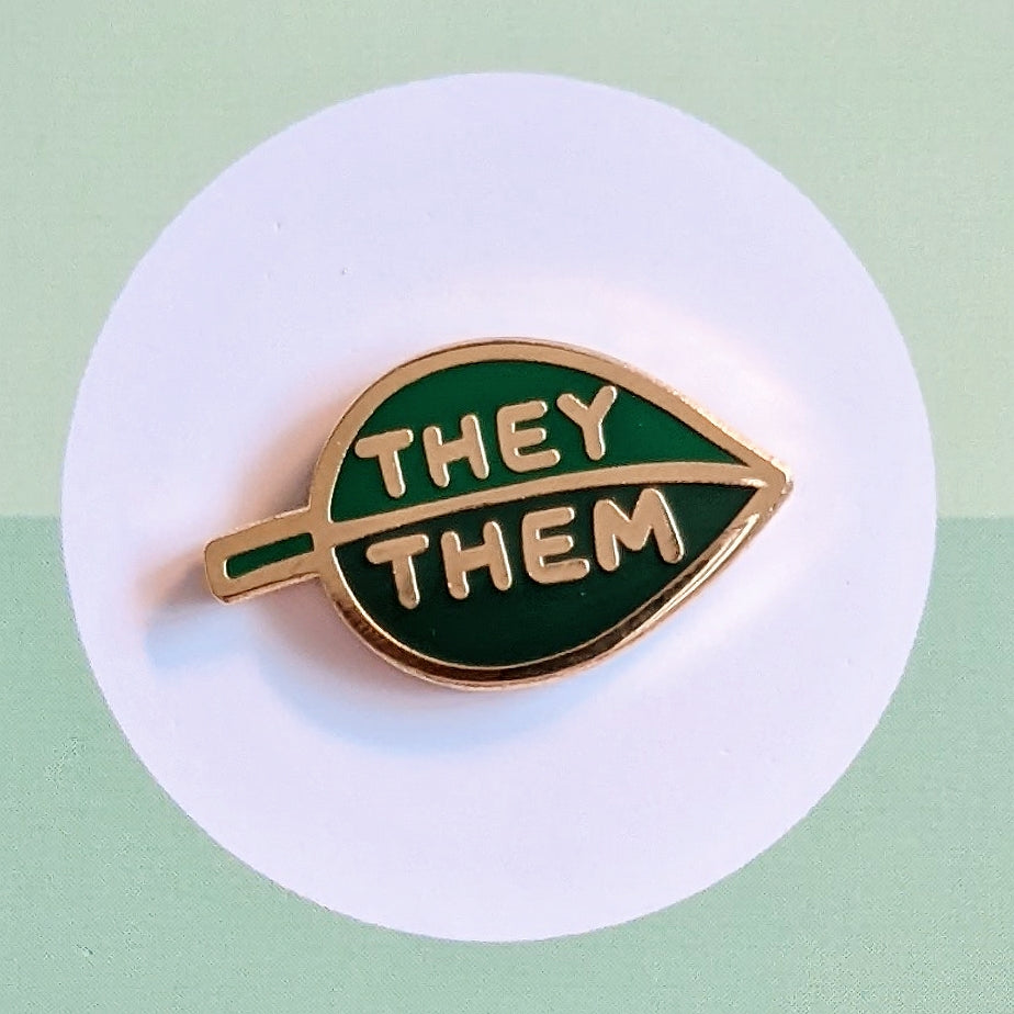 misomomo pronoun enamel pin in the shape of a leaf with two tones of green, with they/them pronouns