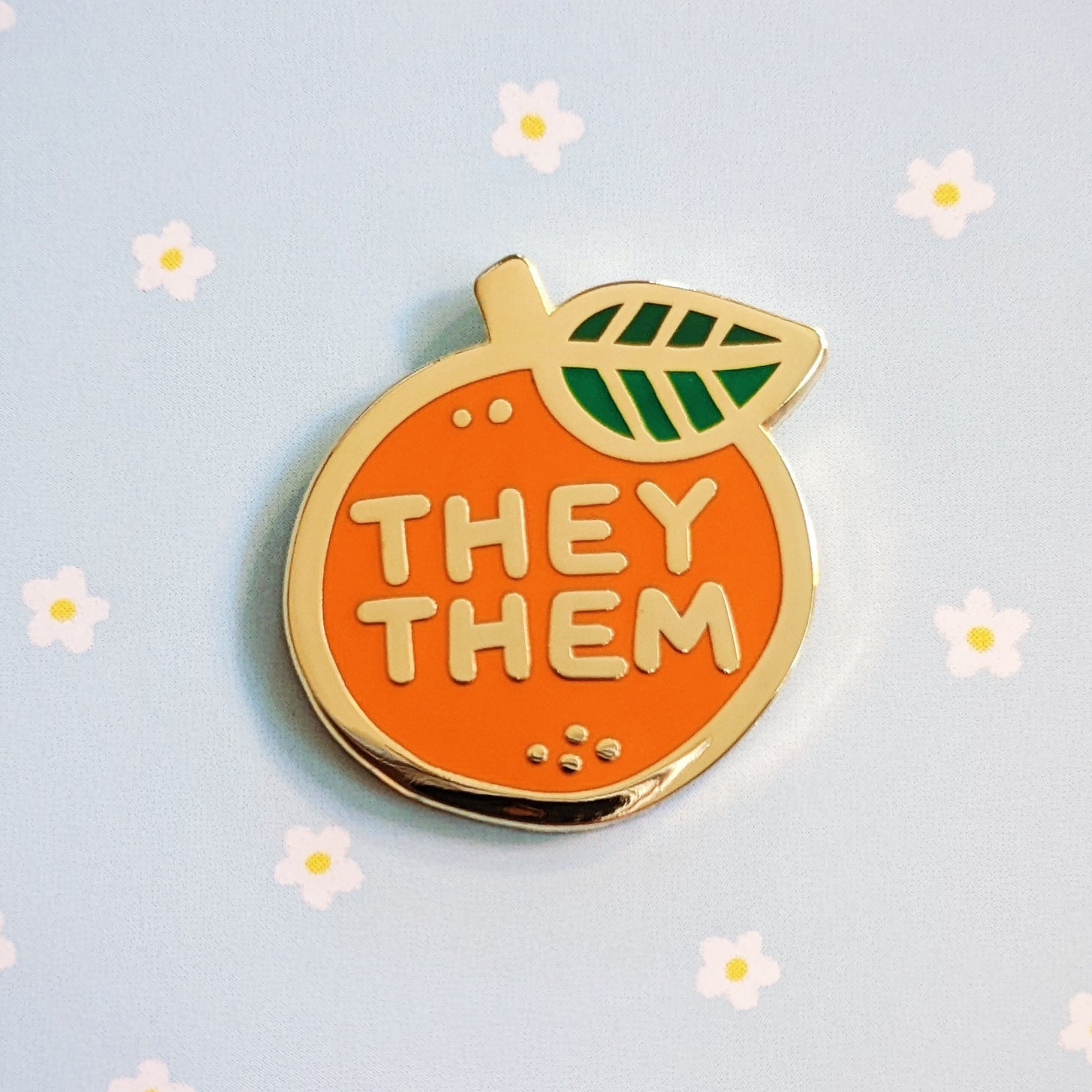misomomo enamel pronoun pride pin in the shape of a cute orange fruit, featuring they/them pronouns